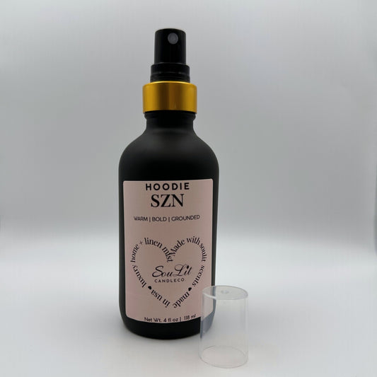 Air and linen freshener mist in 4oz matte black glass bottle with a gold neck with clear top side on white background.