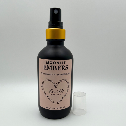 Air and linen freshener mist in 4oz matte black glass bottle with a gold neck and clear top on white background.