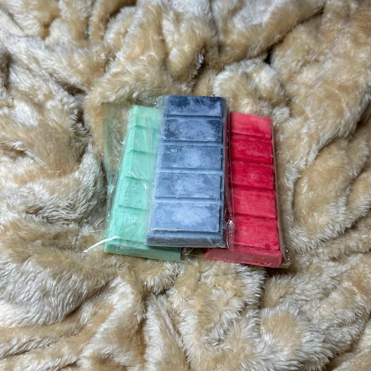 Our trio wax melt bundle includes three different scented wax melt bars (green, charcoal, red) on a textured beige background.