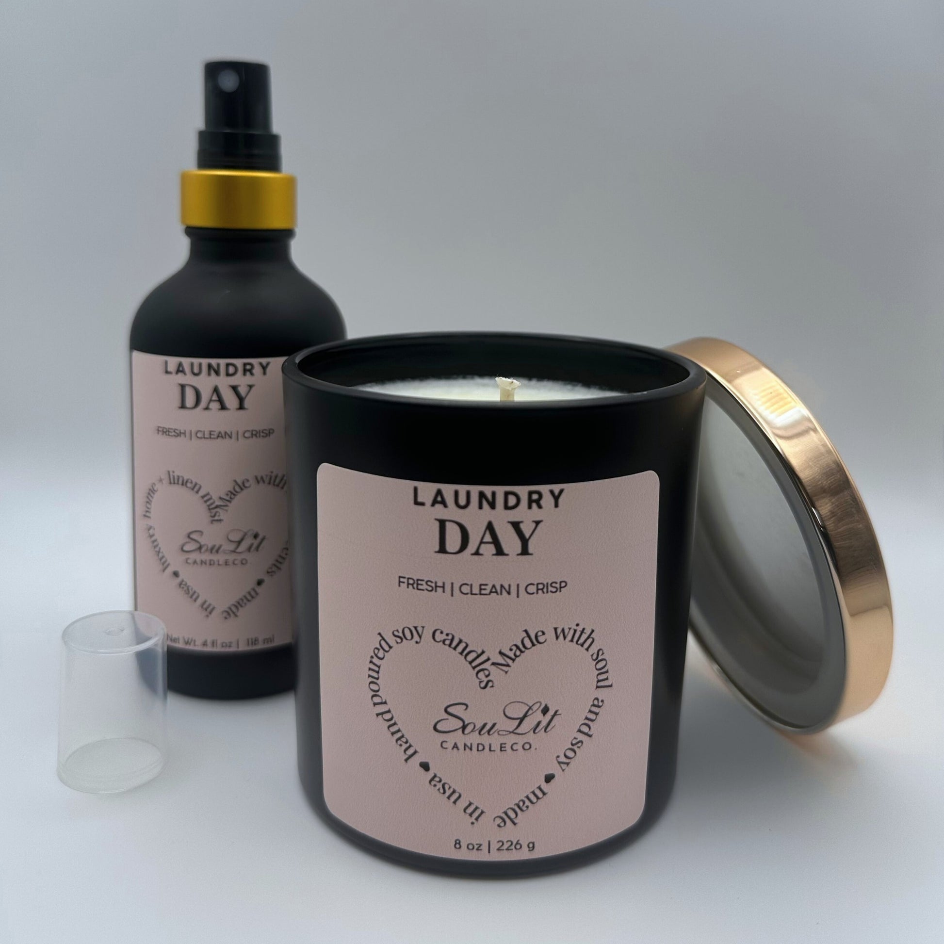 Air and linen mist in 4 oz matte black glass bottle with  gold neck and a Soy candle in 8oz matte black glass jar with rose gold lid off propped on the side of jar on white background. 