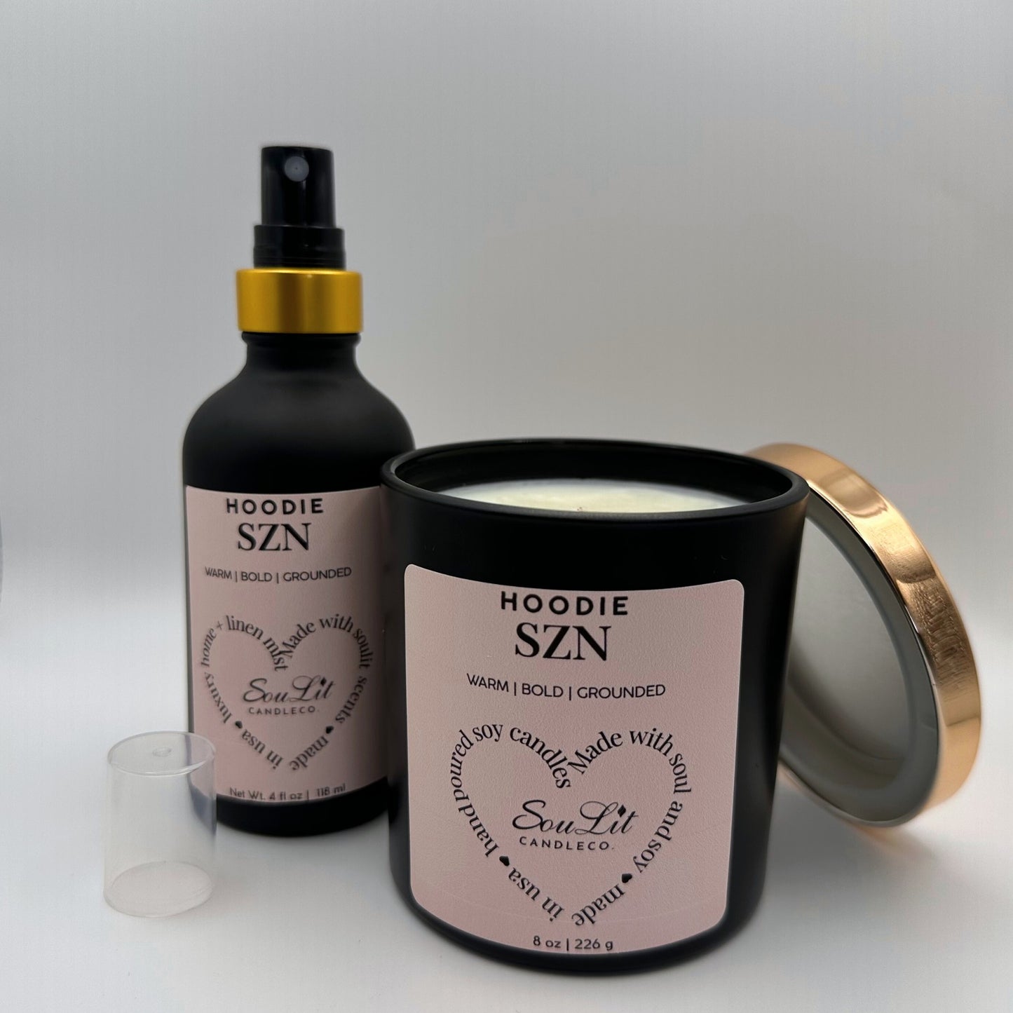Air and linen mist in 4 oz matte black glass bottle with  gold neck and a Soy candle in 8oz matte black glass jar with rose gold lid off propped on the side of jar on white background. 