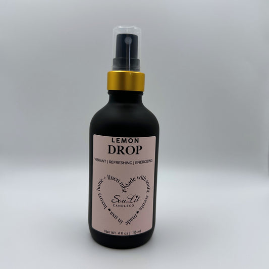 Air and linen freshener mist in 4oz matte black glass bottle with a gold neck and clear top on white background. 