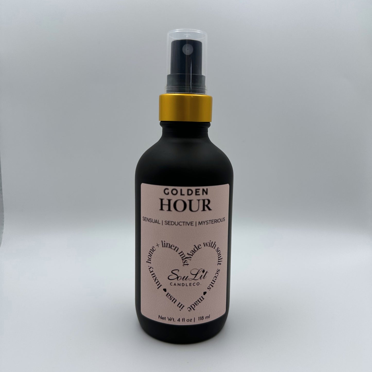 Air and linen freshener mist in 4oz matte black glass bottle with a gold neck and clear top on white background. 