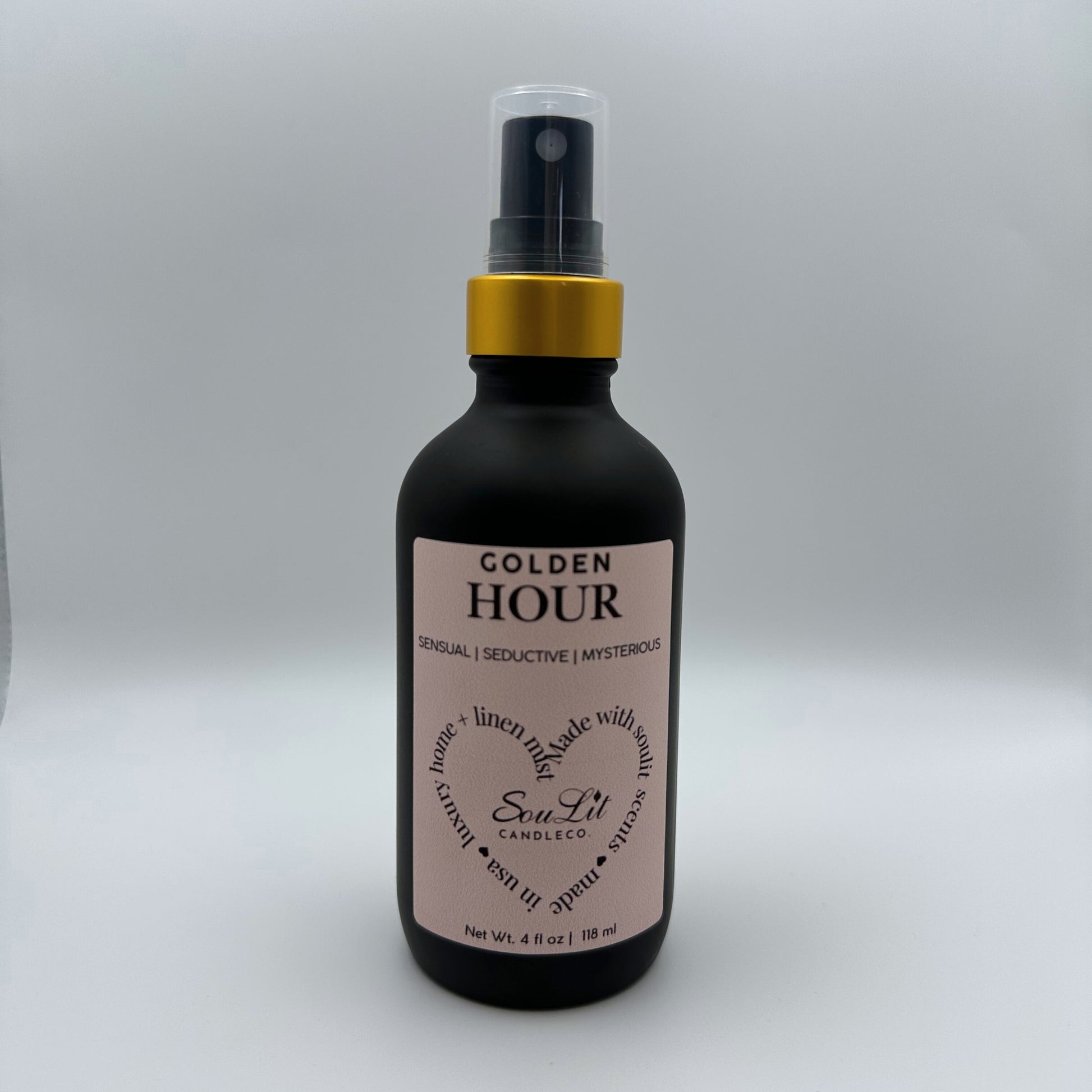 Air and linen freshener mist in 4oz matte black glass bottle with a gold neck and clear top on white background. 