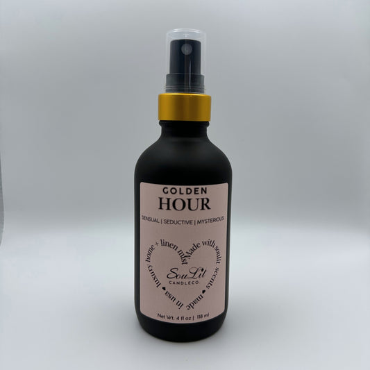Air and linen freshener mist in 4oz matte black glass bottle with a gold neck and clear top on white background. 