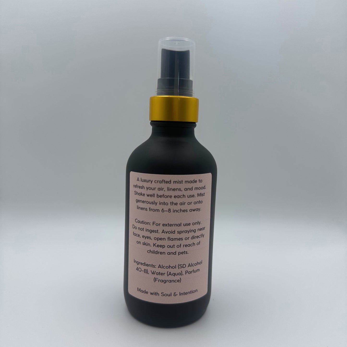 The back of the bottle showing the back label of Air and linen freshener mist in 4oz matte black glass bottle with a gold neck with clear sprayer top on white background. 