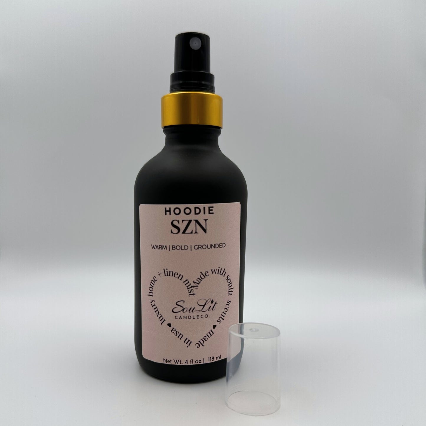 Air and linen freshener mist in 4oz matte black glass bottle with a gold neck with clear top side on white background. 