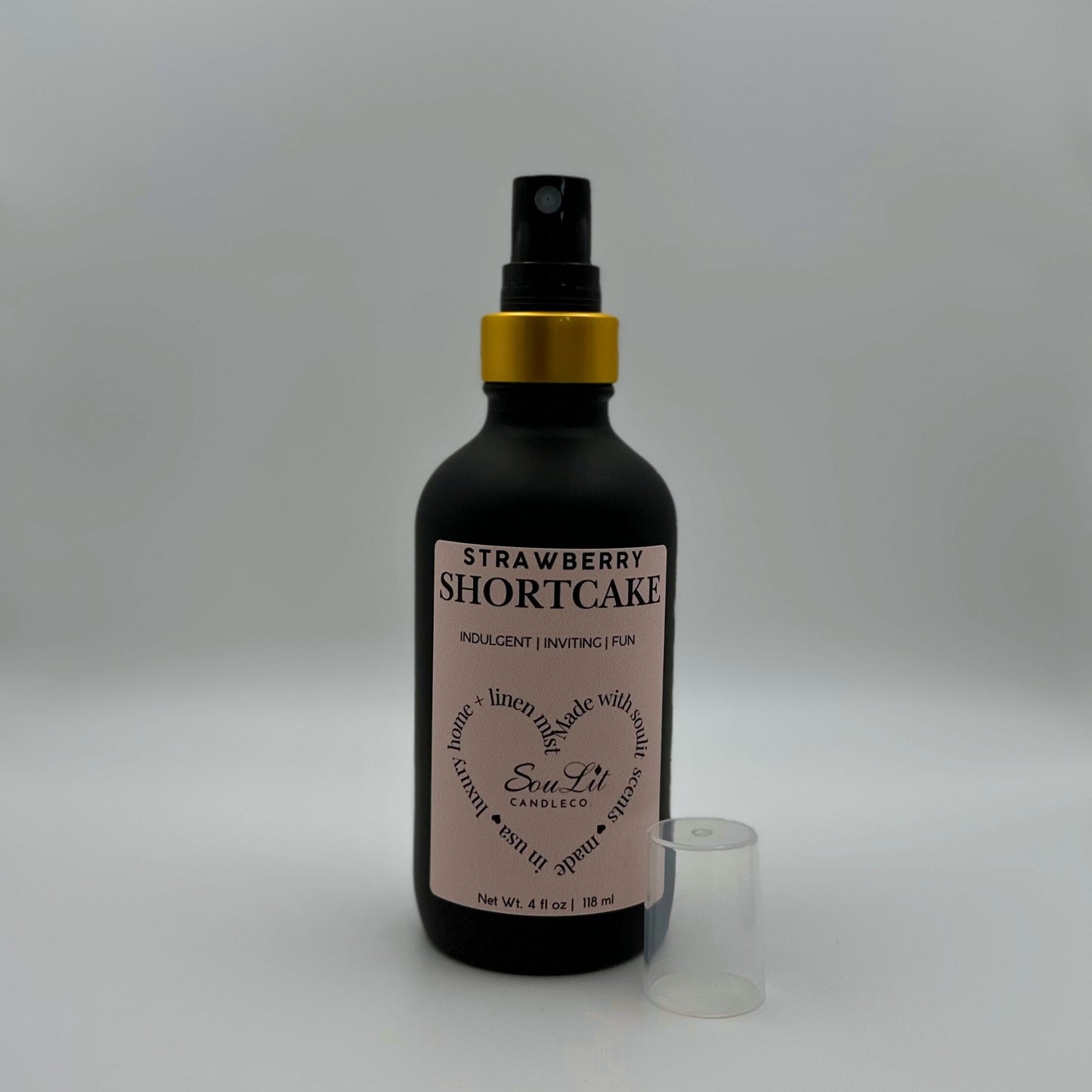 Air and linen freshener mist in 4oz matte black glass bottle with a gold neck with clear top on the side on white background. 