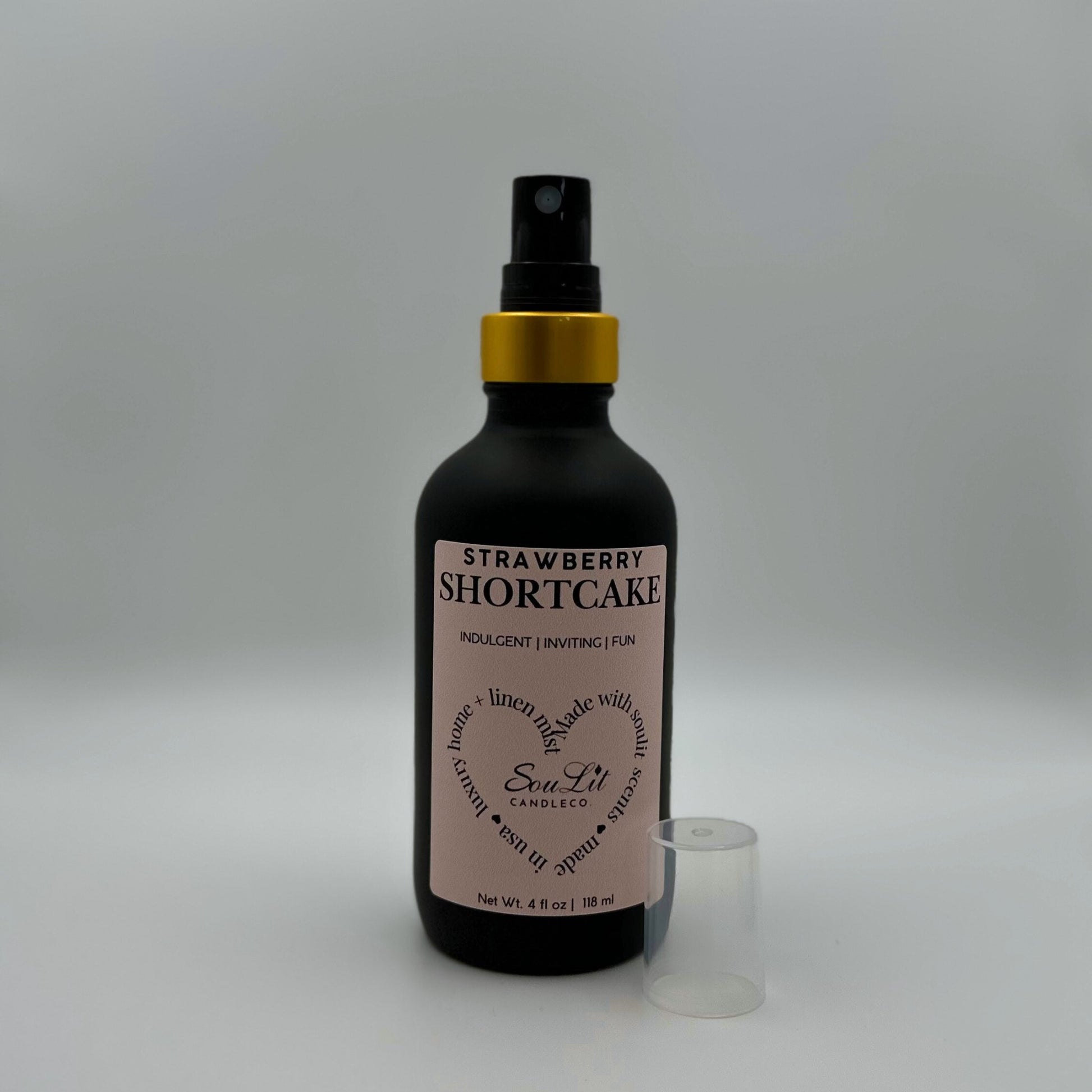 Air and linen freshener mist in 4oz matte black glass bottle with a gold neck with clear top on the side on white background. 