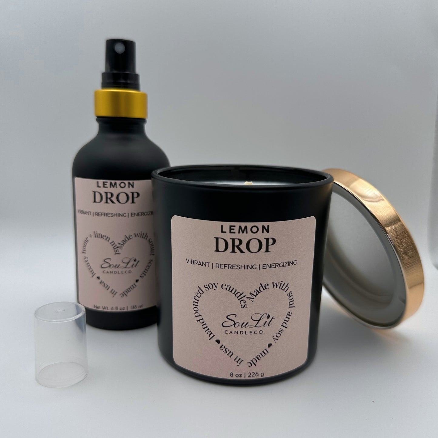Air and linen mist in 4 oz matte black glass bottle with  gold neck and a Soy candle in 8oz matte black glass jar with rose gold lid off propped on the side of jar on white background. 
