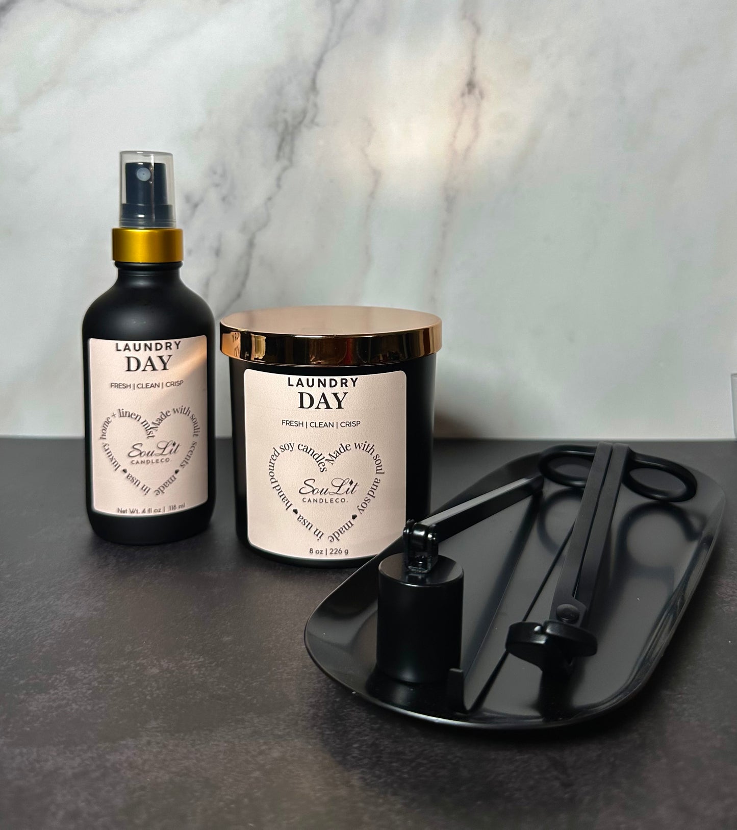 A candle lovers bundle that includes a room and linen mist in a 4oz glass bottle with gold neck, soy candle in a 8oz matte black jar with rose gold lid, and a black semi-gloss wick trimmer, sniffer, dipper and tray set. 