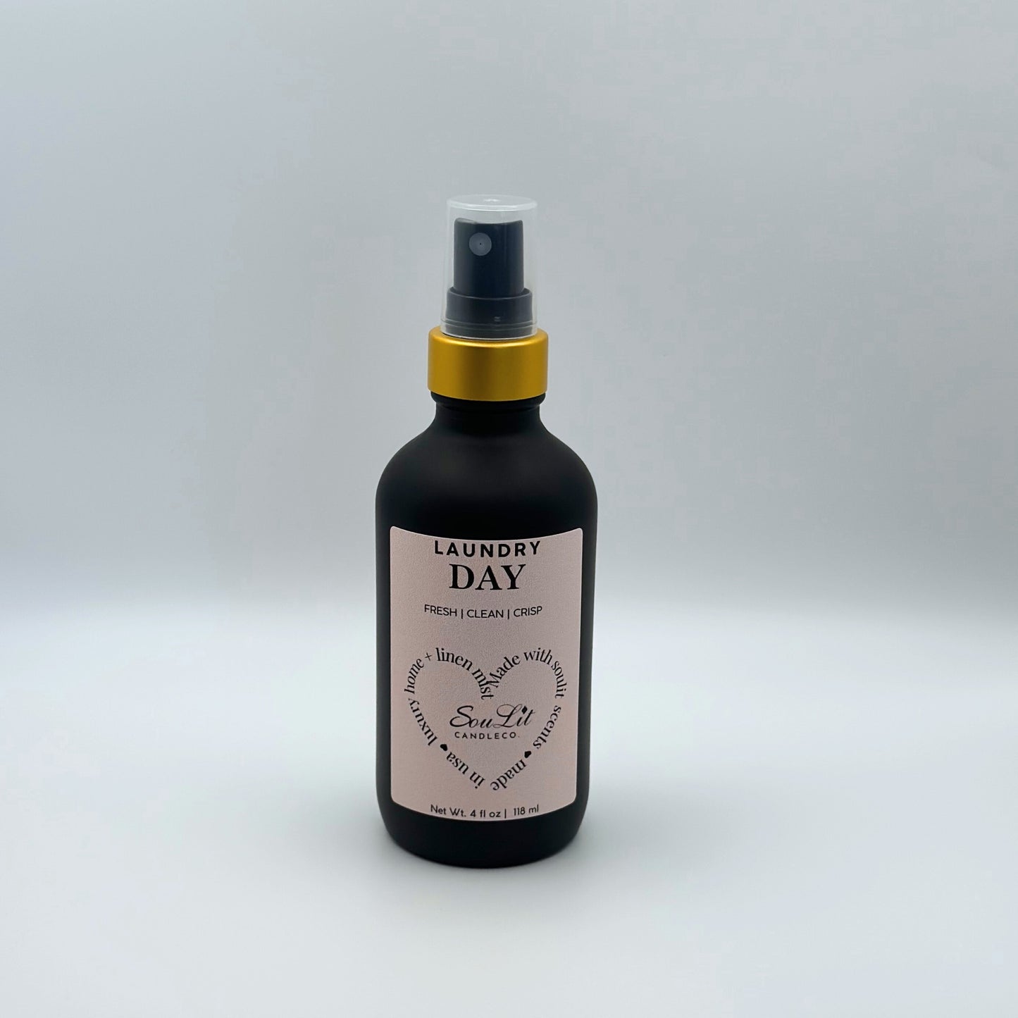 Air and linen freshener mist in 4oz matte black glass bottle with a gold neck and clear top on white background. 