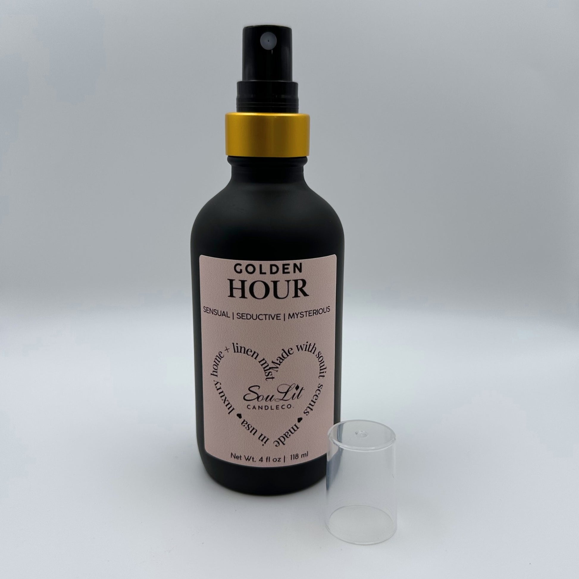 Air and linen freshener mist in 4oz matte black glass bottle with a gold neck with clear top on side on white background. 