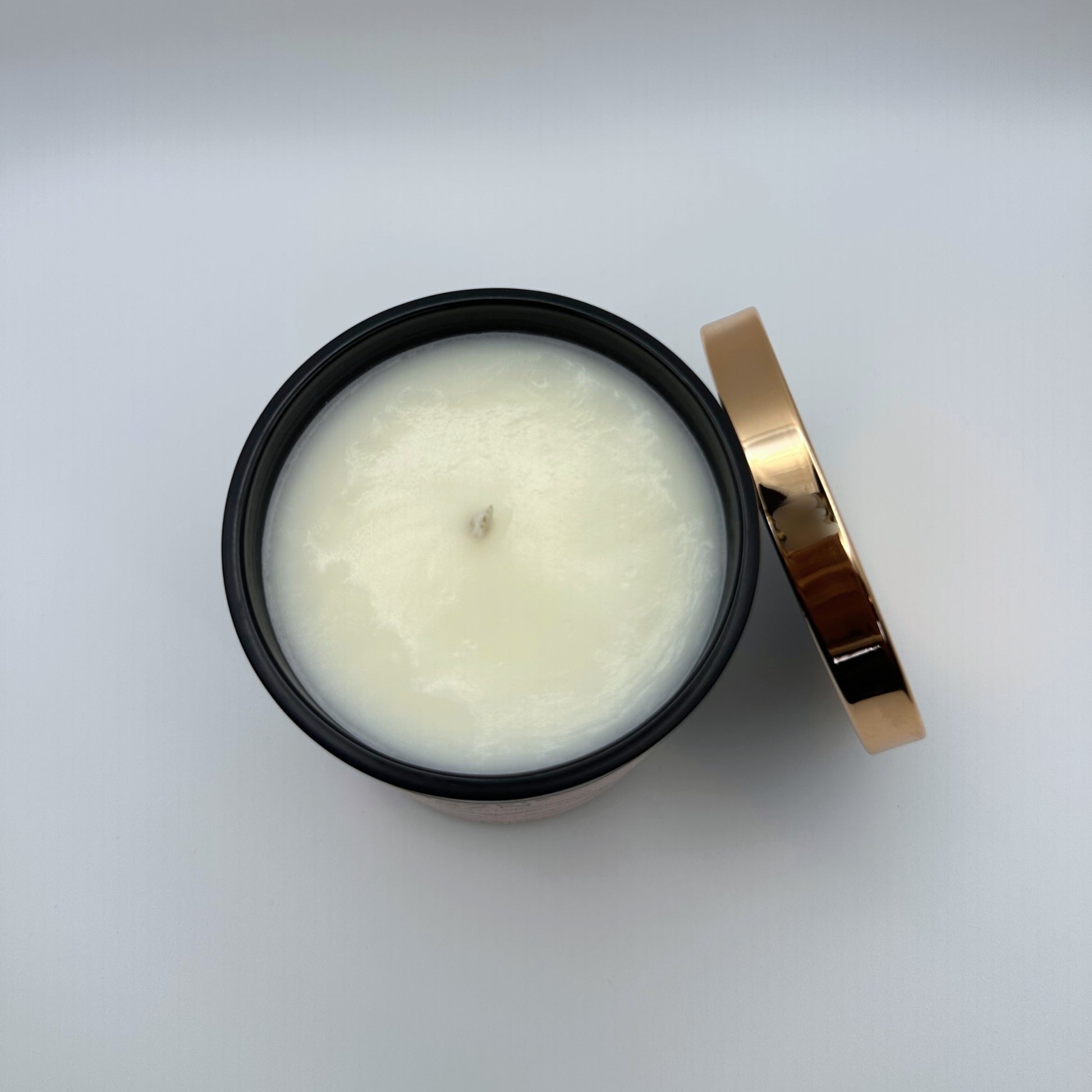 Top down view of soy candle in black jar and rose gold lid propped on the side. 