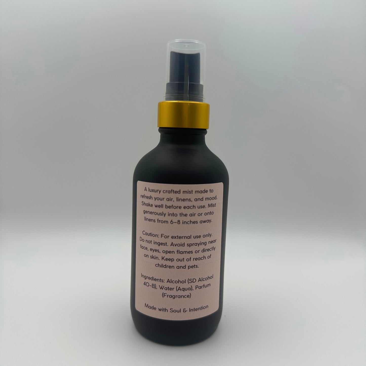 The back of the bottle showing the back label of Air and linen freshener mist in 4oz matte black glass bottle with a gold neck with clear sprayer top on white background. 