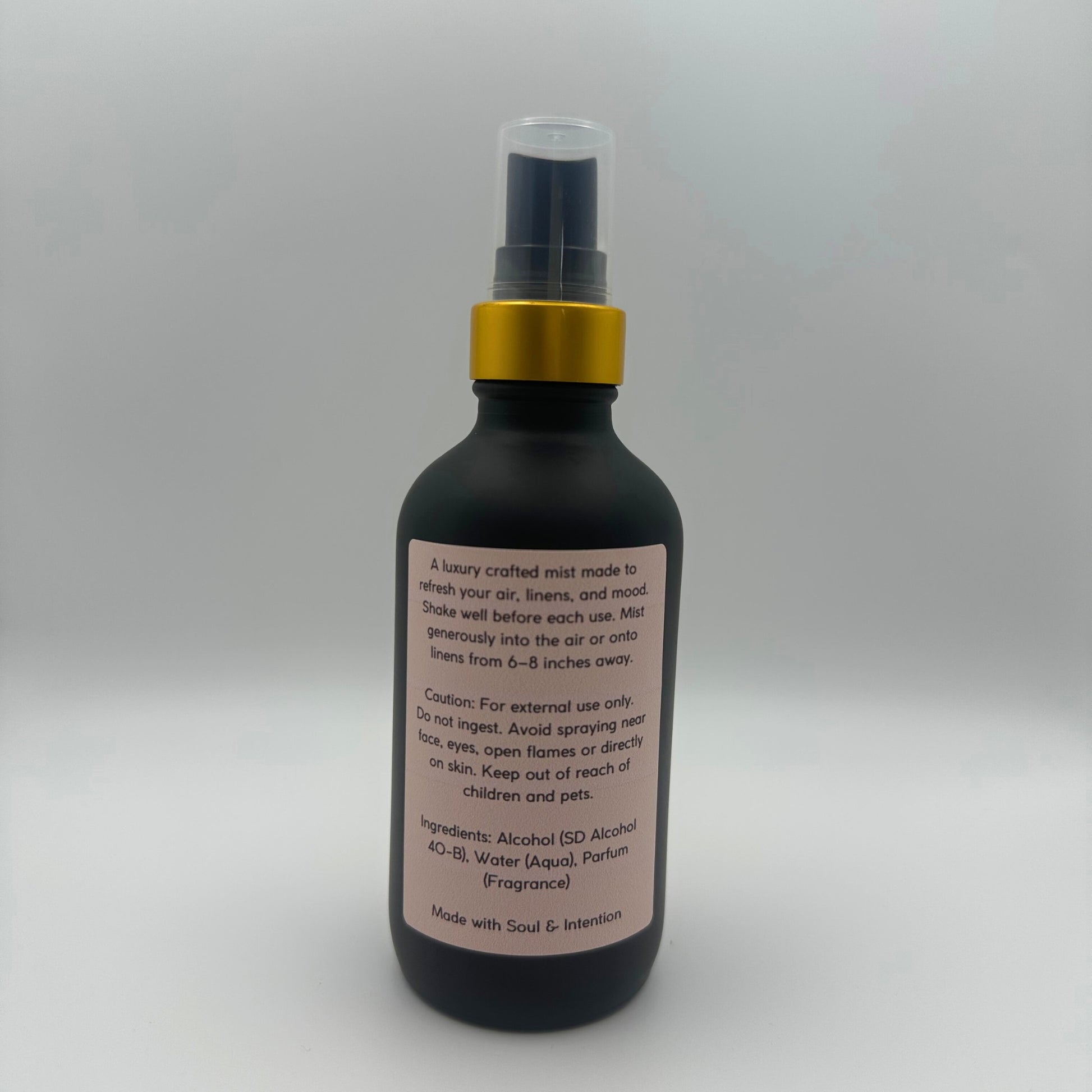 The back of the bottle showing the back label of Air and linen freshener mist in 4oz matte black glass bottle with a gold neck with clear sprayer top on white background. 