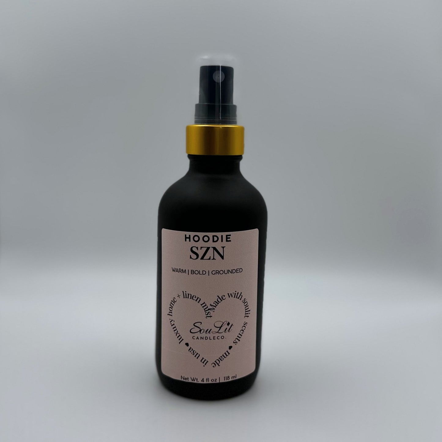 Air and linen freshener mist in 4oz matte black glass bottle with a gold neck and clear top on white background. 