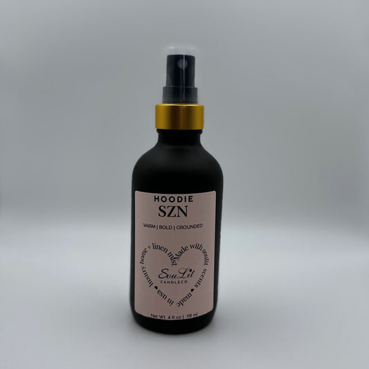 Air and linen freshener mist in 4oz matte black glass bottle with a gold neck and clear top on white background. 