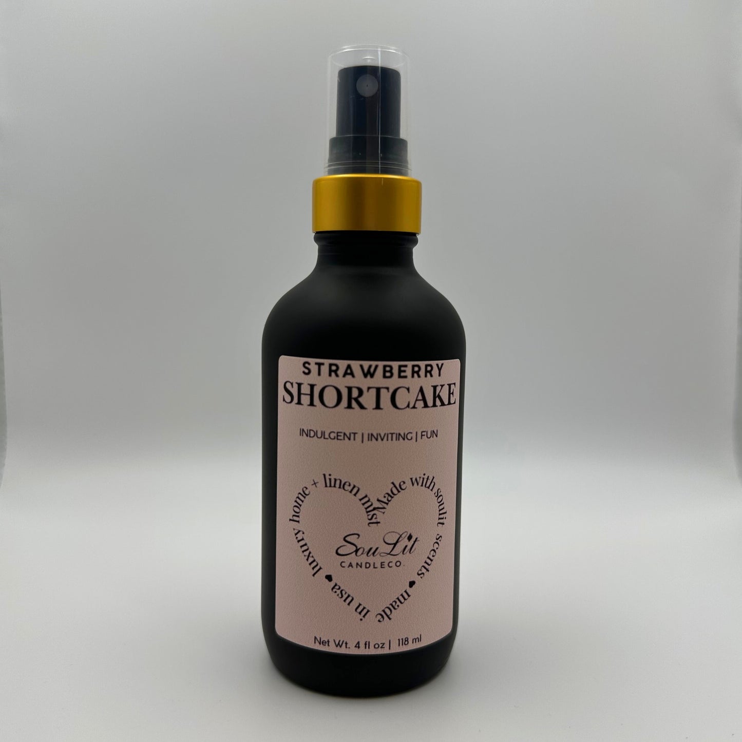 Air and linen freshener mist in 4oz matte black glass bottle with a gold neck and clear top on white background. 