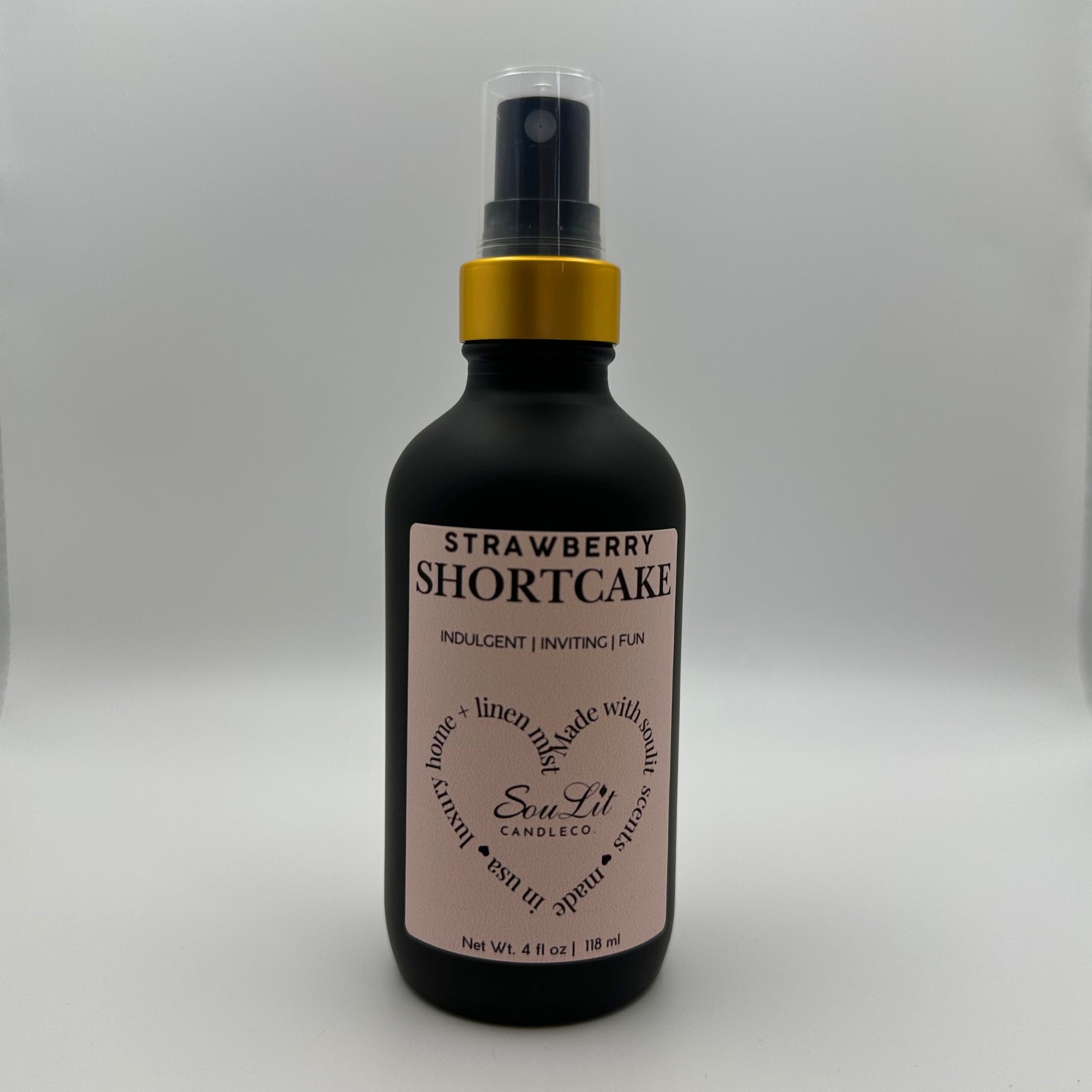 Air and linen freshener mist in 4oz matte black glass bottle with a gold neck and clear top on white background. 