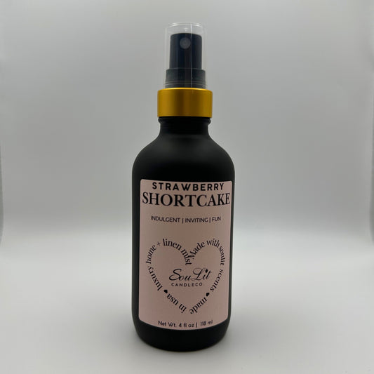 Air and linen freshener mist in 4oz matte black glass bottle with a gold neck and clear top on white background. 