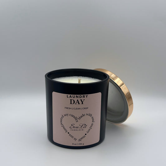 Soy candle in 8oz matte black glass jar with rose gold lid off propped on the side of jar on white background. 