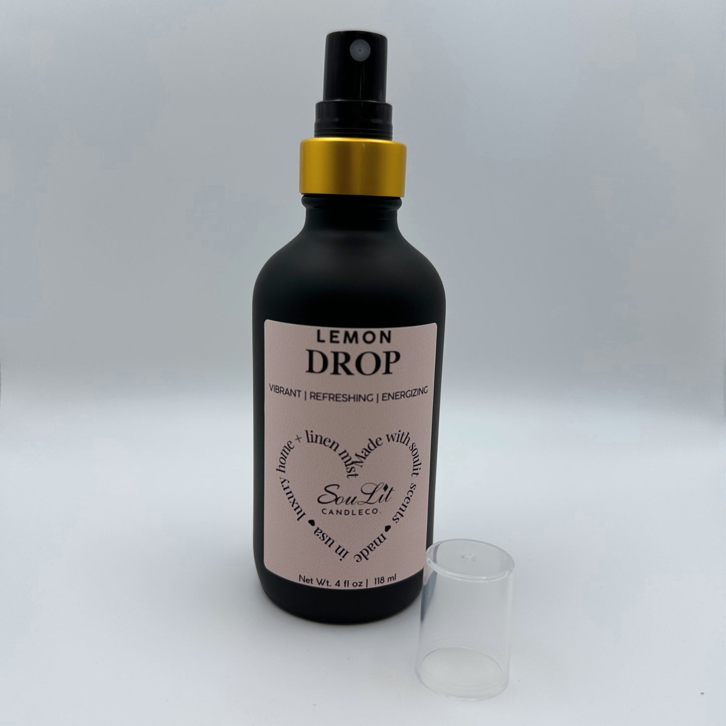 Air and linen freshener mist in 4oz matte black glass bottle with a gold neck with clear sprayer top on the side on white background. 