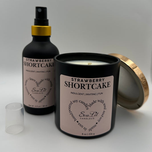 Air and linen mist in 4 oz matte black glass bottle with  gold neck and a Soy candle in 8oz matte black glass jar with rose gold lid off propped on the side of jar on white background. 