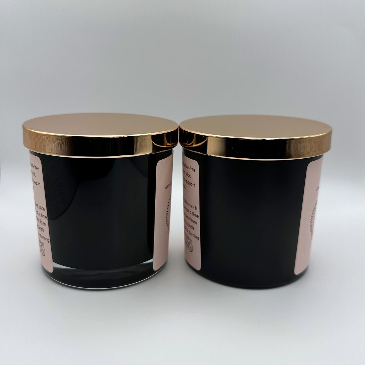 Two Soy candles, one in a 8oz matte black glass jar with rose gold lid and one in a 8oz gloss black jar on white background. 