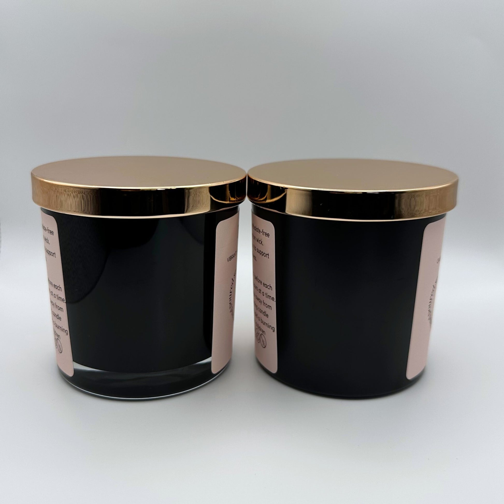 Two Soy candles, one in a 8oz matte black glass jar with rose gold lid and one in a 8oz gloss black jar on white background. 