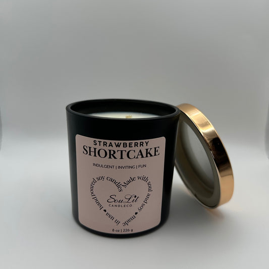 Soy candle in 8oz matte black glass jar with rose gold lid off propped on the side of jar on white background. 