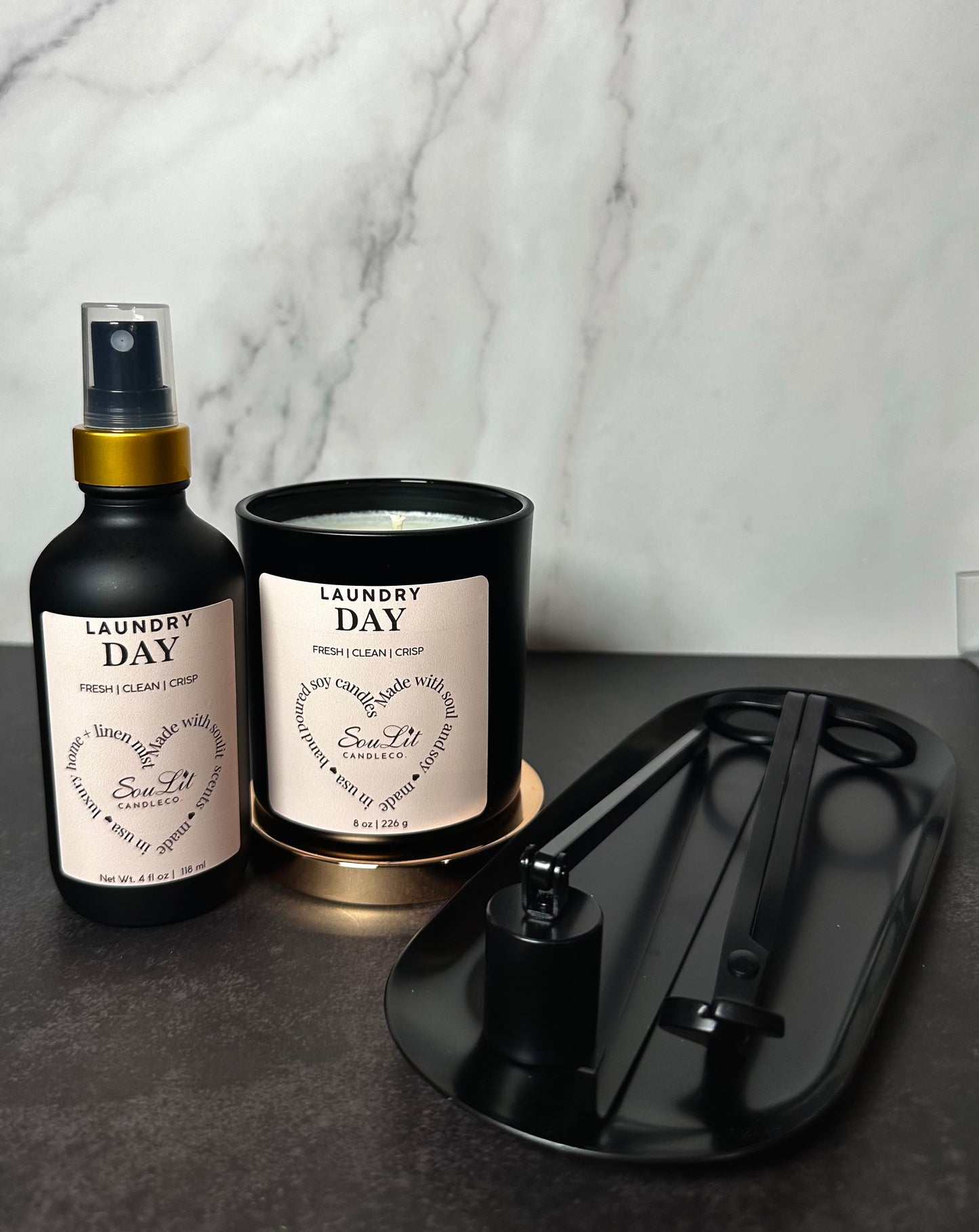 A candle lovers bundle that includes a room and linen mist in a 4oz glass bottle with gold neck, soy candle in a 8oz matte black jar with rose gold lid, and a black semi-gloss wick trimmer, sniffer, dipper and tray set. 
