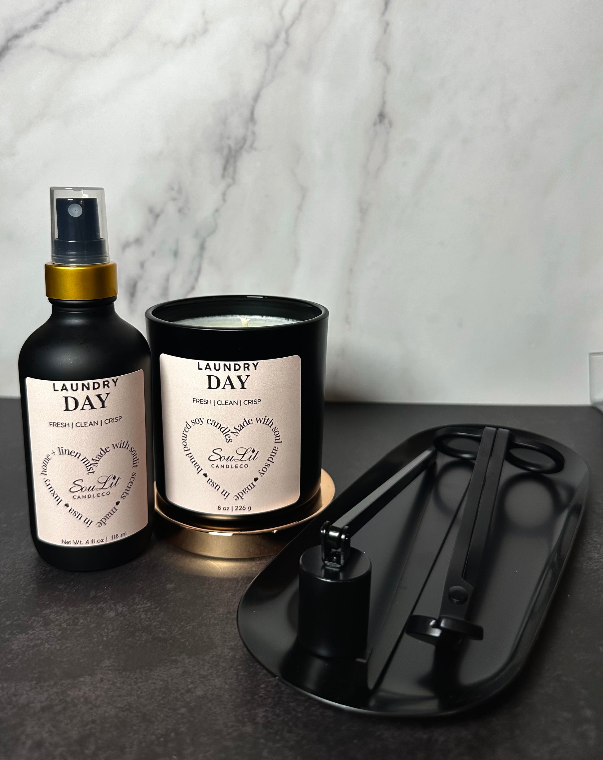 A candle lovers bundle that includes a room and linen mist in a 4oz glass bottle with gold neck, soy candle in a 8oz matte black jar with rose gold lid, and a black semi-gloss wick trimmer, sniffer, dipper and tray set. 