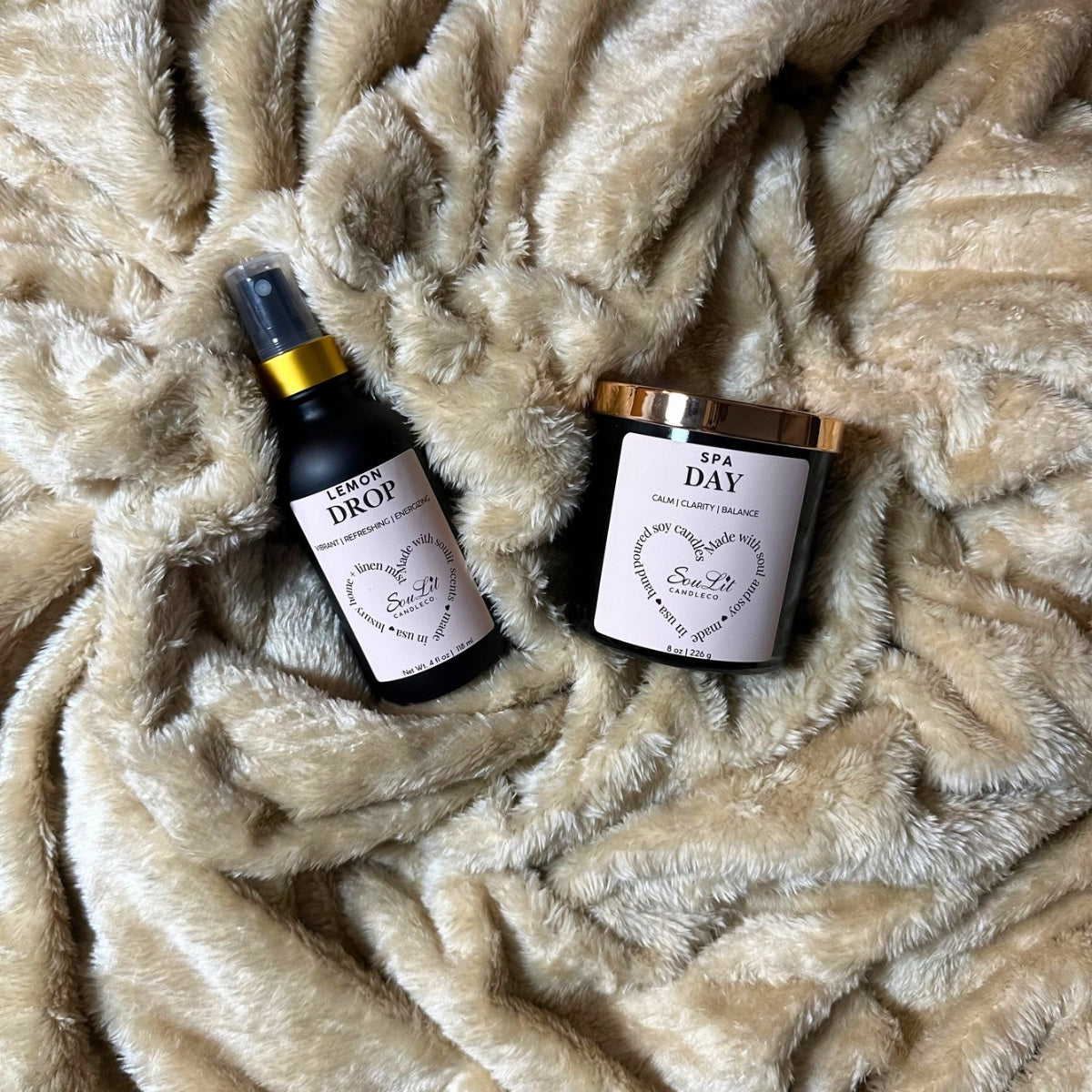 Our Soullit Essentials Bundle includes an Air and linen mist in a 4oz matte black glass bottle with gold neck and a soy candle in an 8oz matte black glass jar on a texture beige background. 